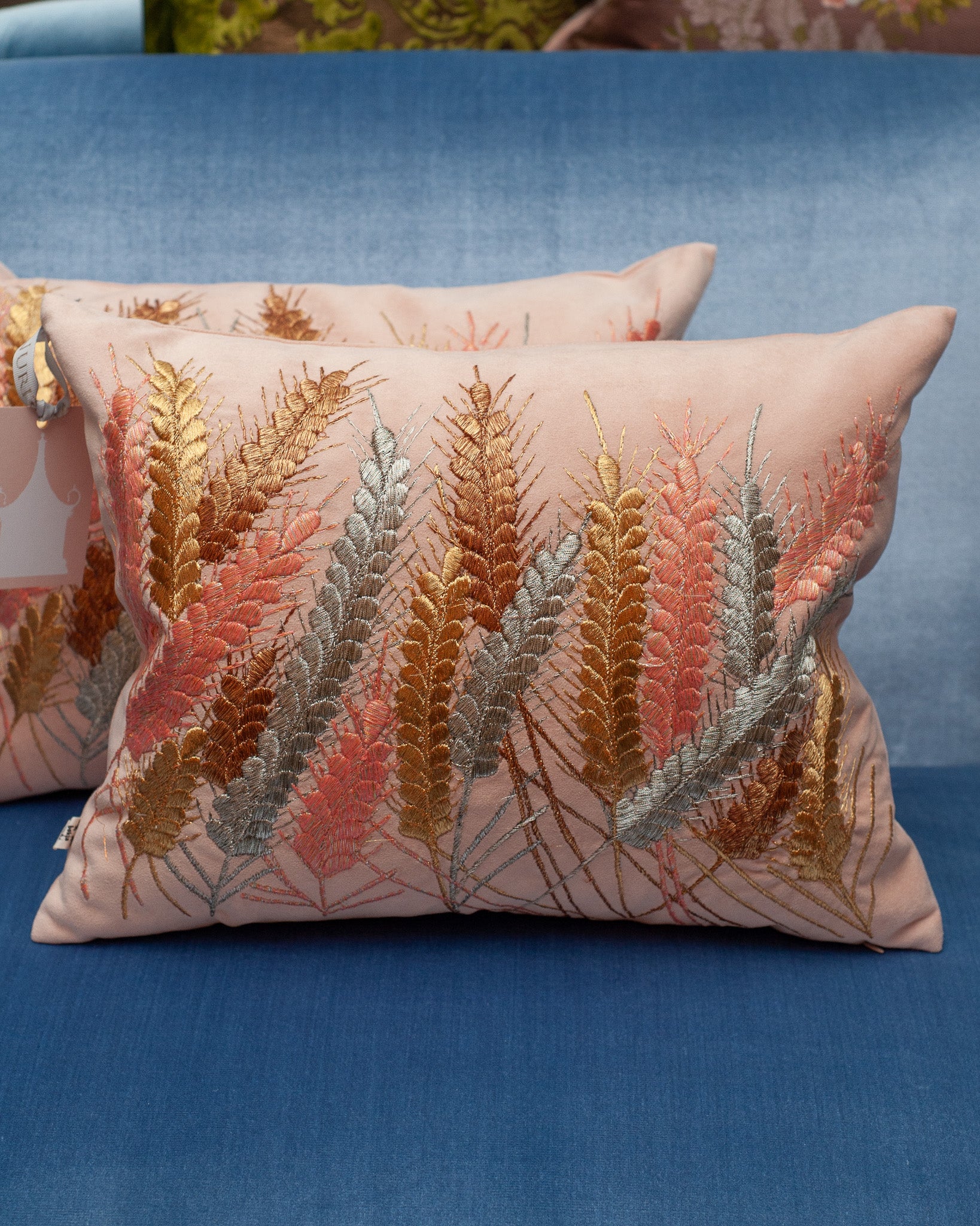A CONTEMPORARY EMBROIDERED PILLOW ON SOFT PINK ULTRASUEDE WITH METALLIC WHEAT