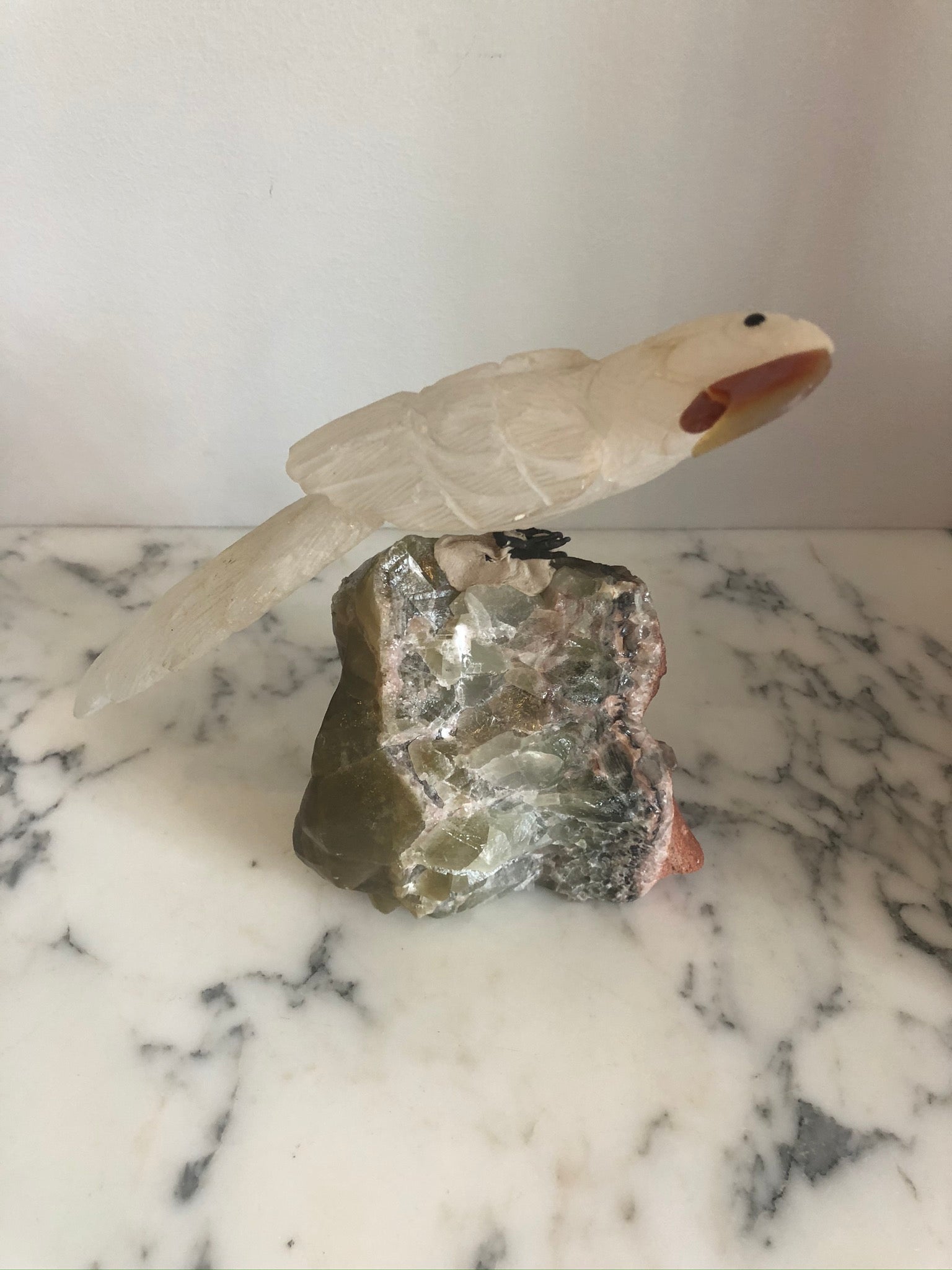 A carved rock crystal bird on a natural quartz base in a cloche.