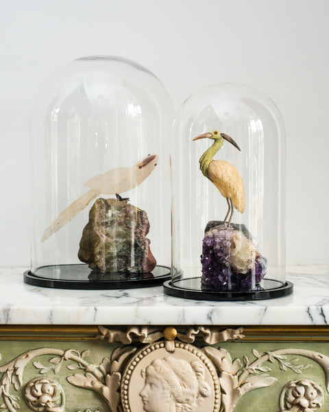 A semi-precious carved crane perched on a large Amethyst rock in a cloche.