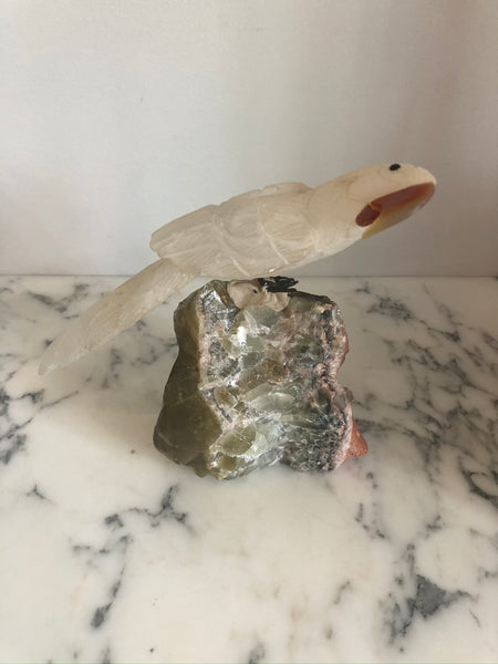 A carved rock crystal bird on a natural quartz base in a cloche.