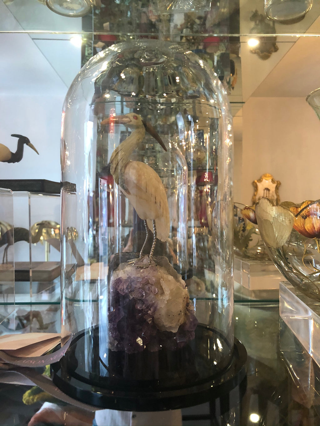 A semi-precious carved crane perched on a large Amethyst rock in a cloche.