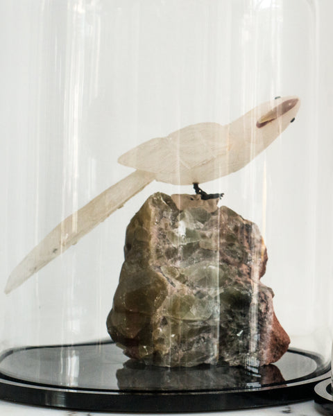 A carved rock crystal bird on a natural quartz base in a cloche.