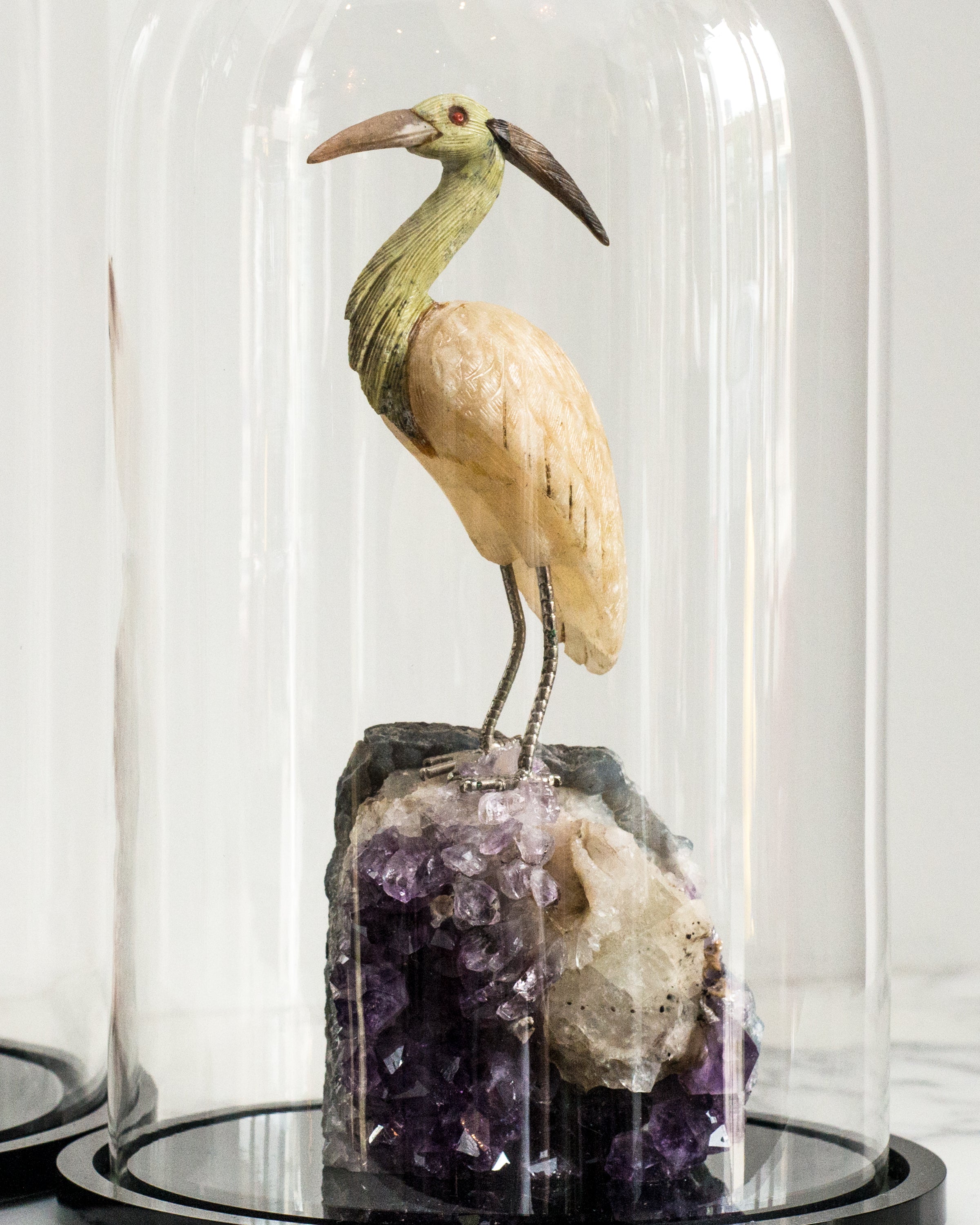 A semi-precious carved crane perched on a large Amethyst rock in a cloche.