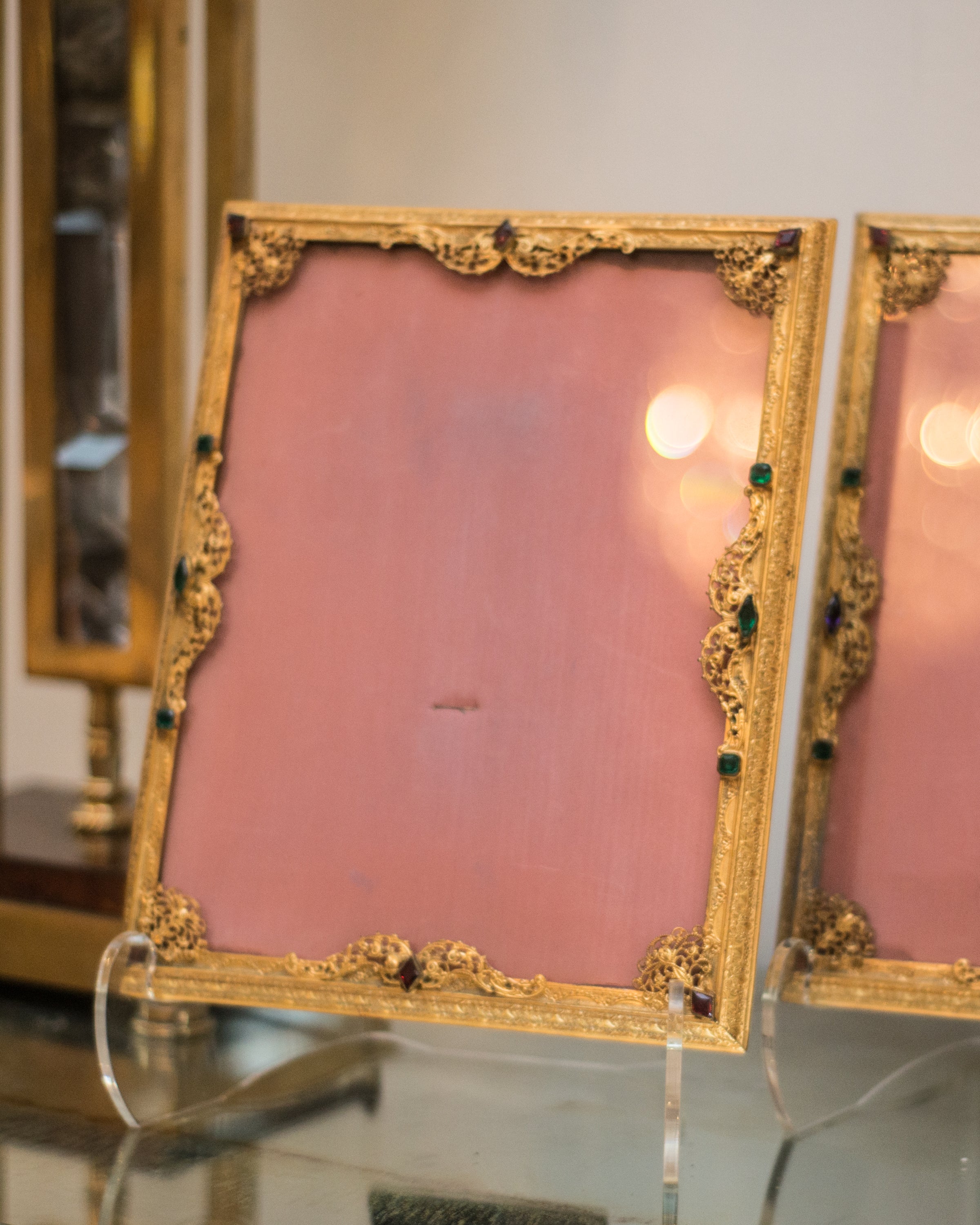 An antique gold picture frame with filigree work and jewels backed in pink silk moiré.