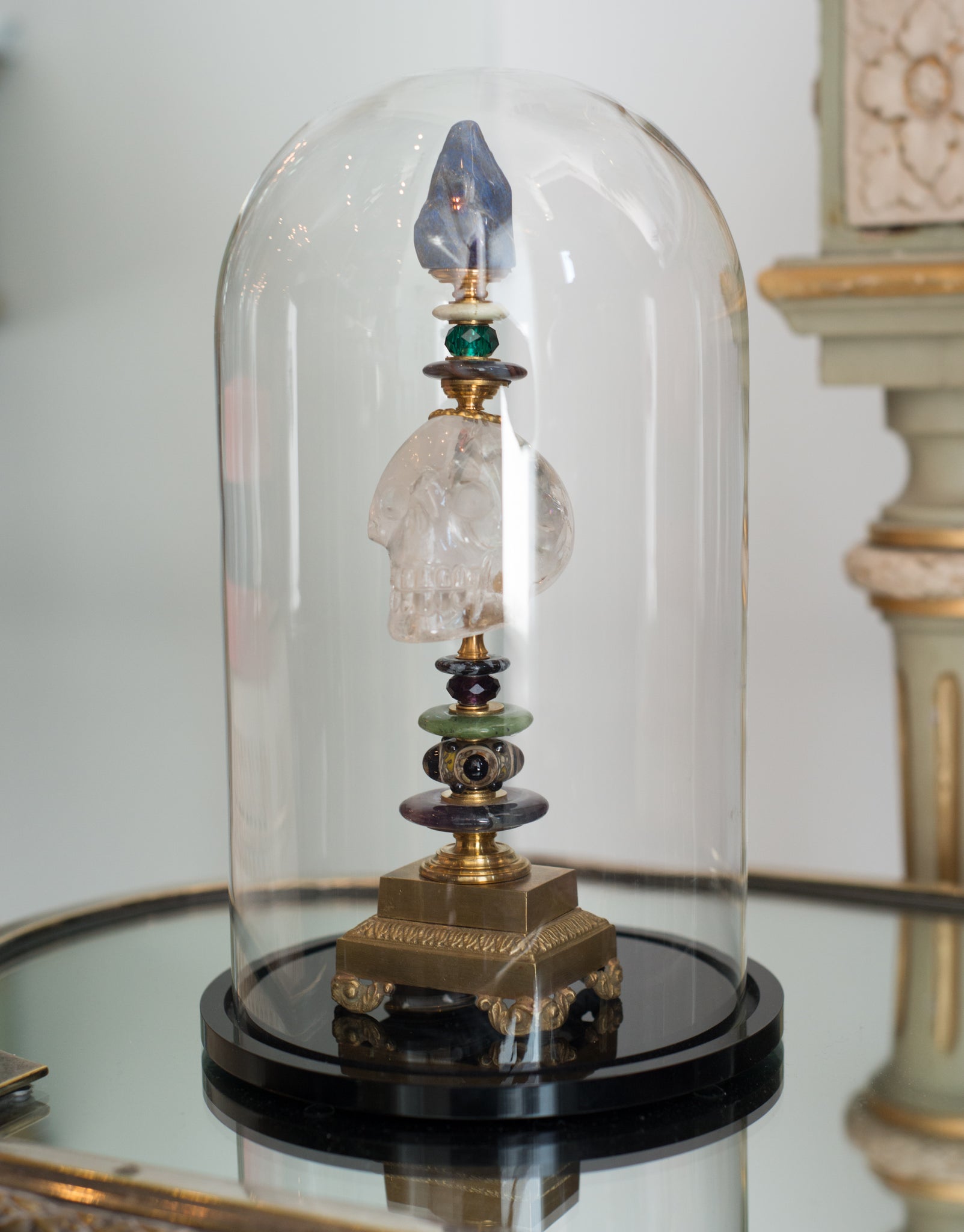 A one of a kind sculptural objet consisting of a carved Rock Crystal skull with  semi-precious stones and antique bronze components on a bronze pedestal by German artist, Dupont. At Maison Nurita we try and elevate our accessories by placing them on a cube or enclosing them in a dome.