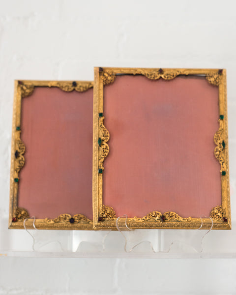An antique gold picture frame with filigree work and jewels backed in pink silk moiré.