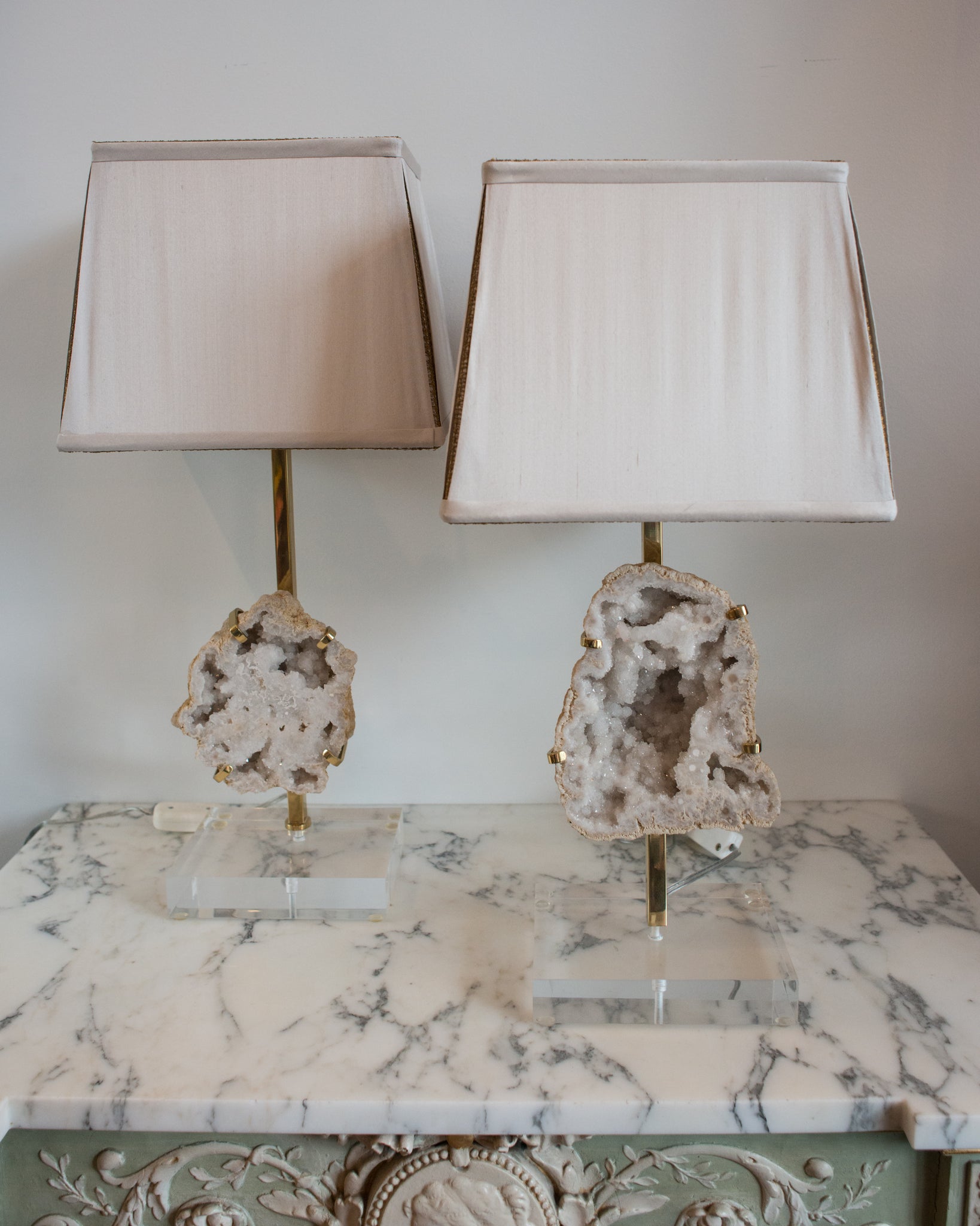 Simple yet striking, these lamps contain large sliced quartz stones which are held in place by simple bronze claws resembling a ring setting. These lamps are finished with hand made silk shades with vintage metallic gold trim and sit atop thick acrylic bases. Sold as a pair.